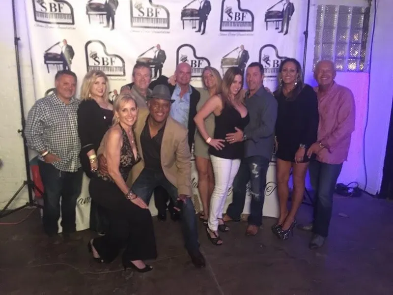 Eleven guests pose together in front of a Shawn Brown Foundation logo backdrop at an evening event